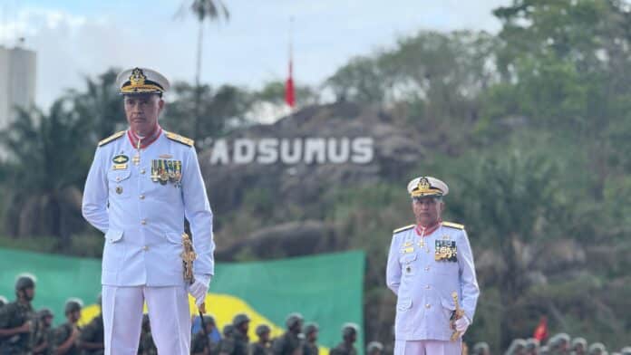 Oficiais navais em cerimônia militar, inscrições no fundo.