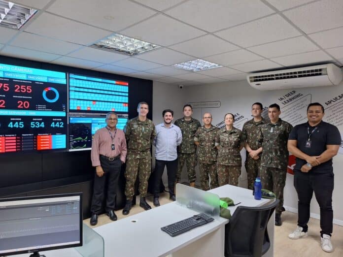 Pessoas em uniforme militar em frente a painéis digitais.