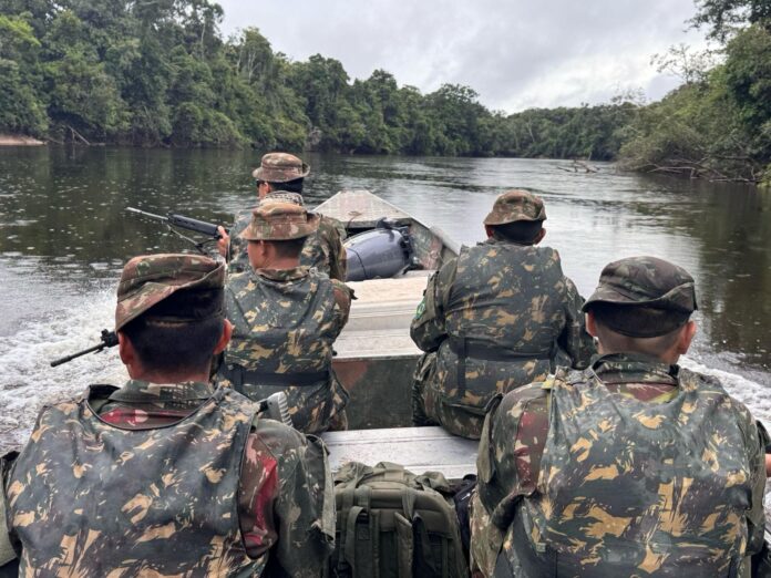 Soldados em barco navegando rio na Amazônia.
