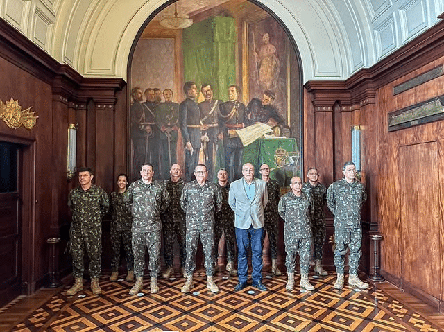 Militares em sala com pintura histórica.
