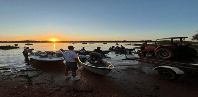 Pôr do sol, barcos e trator em lagoa.