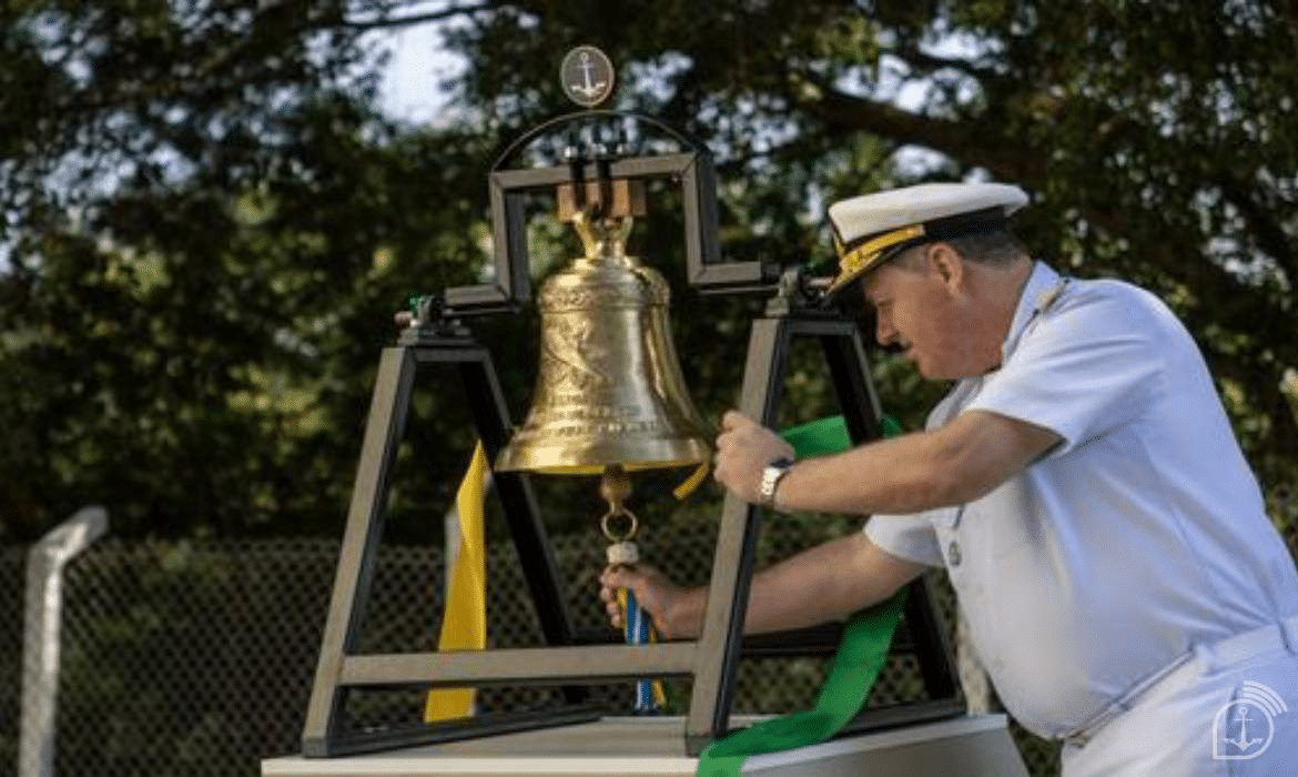 Oficial naval toca sino cerimonial ao ar livre.