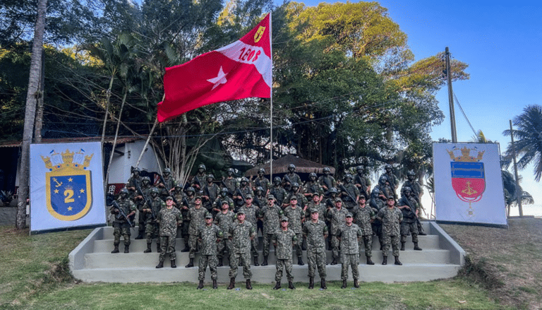 Soldados em formação com bandeira vermelha ao fundo.