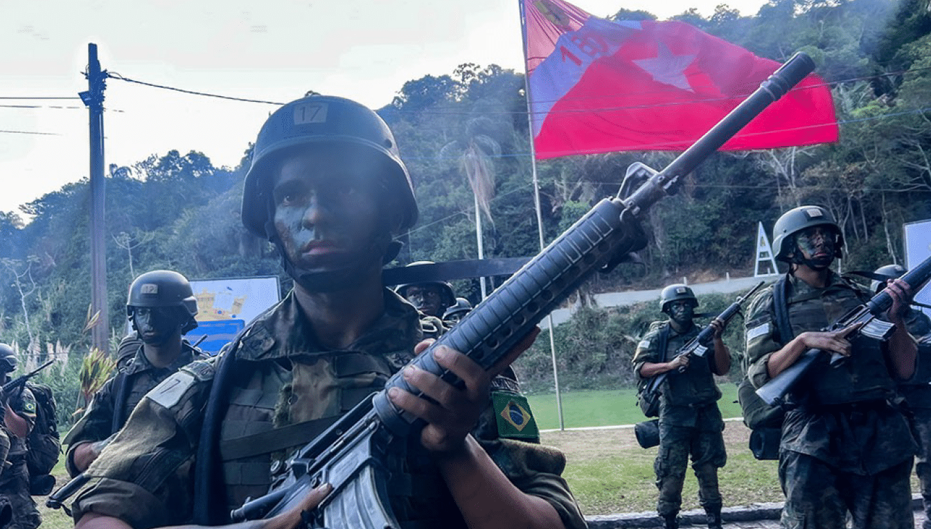 Soldados camuflados em treinamento com bandeira ao fundo.