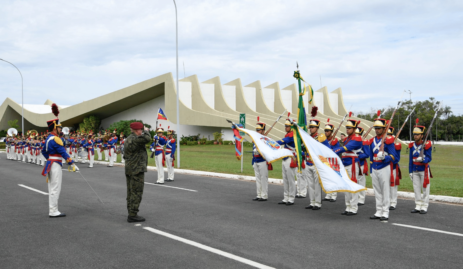 Desfile militar em frente a prédio moderno.