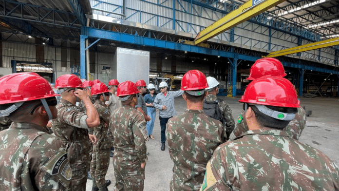 Militares em inspeção na fábrica com capacetes vermelhos.