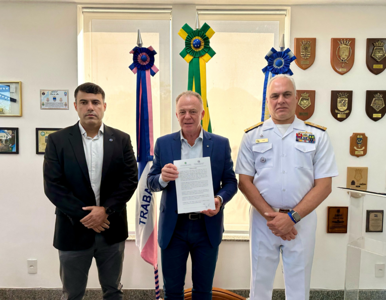 Três homens em uniforme militar e social posam em escritório.