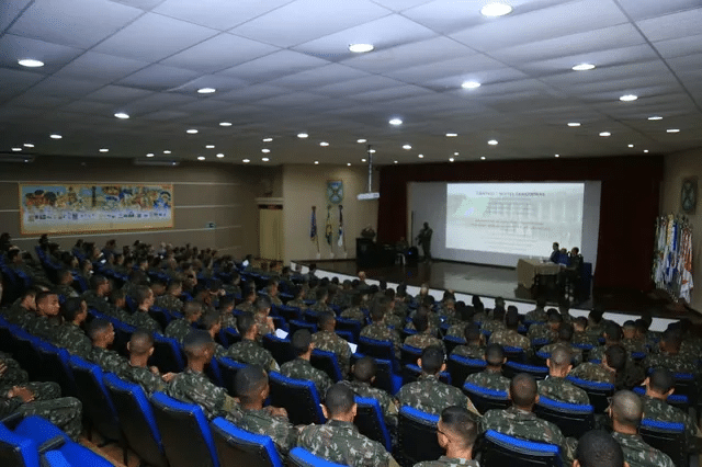 Militares em auditório assistem a apresentação em telão.
