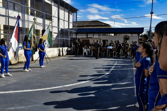 Cerimônia cívica com hinos e bandeiras em escola.