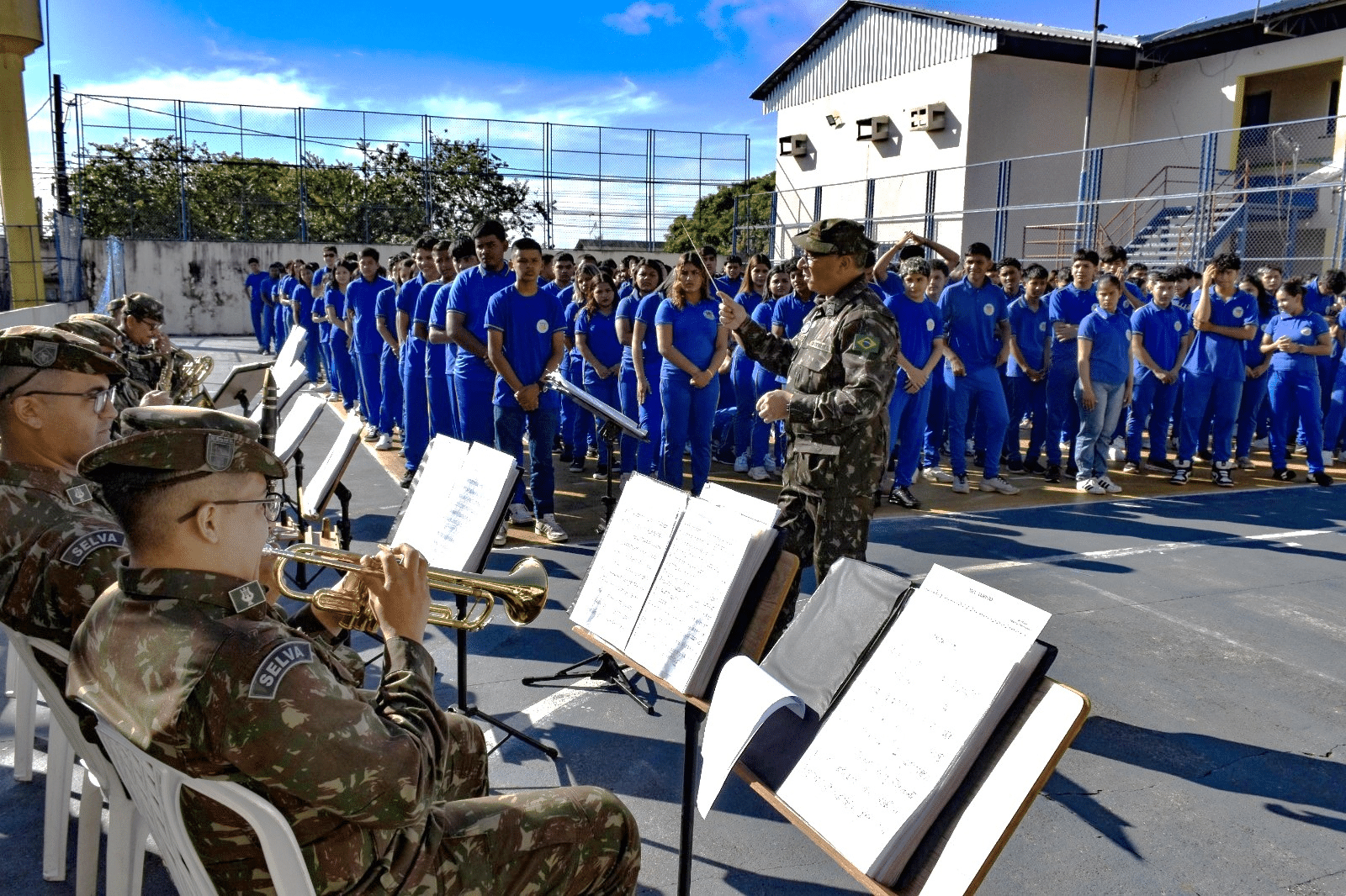 Orquestra militar tocando para estudantes uniformizados.