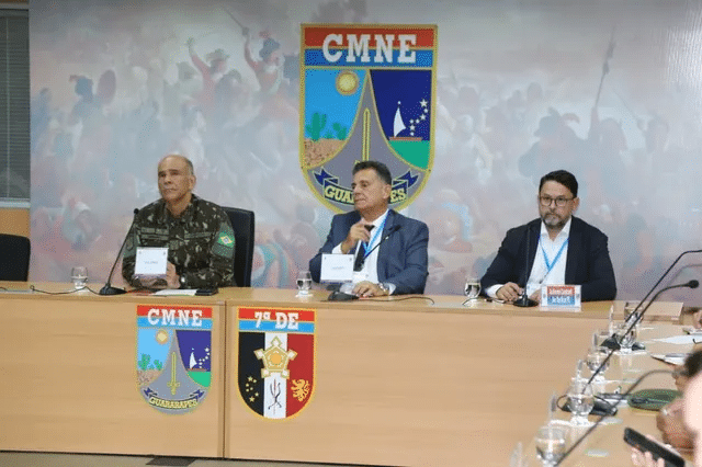 Reunião do CMNE com oficiais e autoridades em mesa.