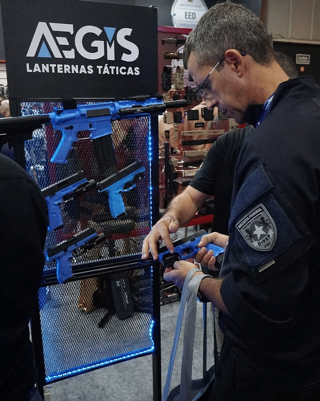 Homem examina arma azul em estande de exposição.