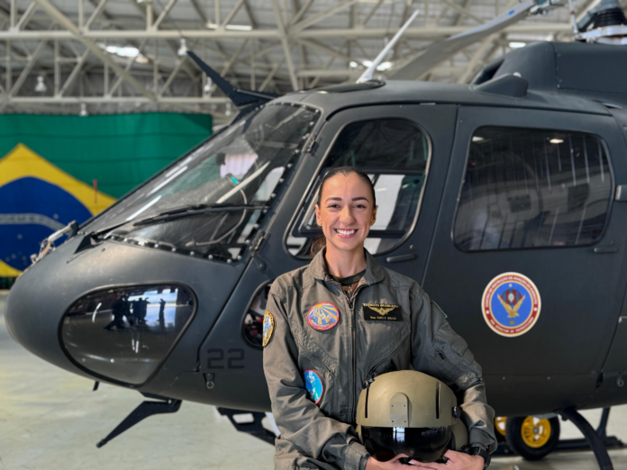 Piloto militar sorrindo em frente a helicóptero.