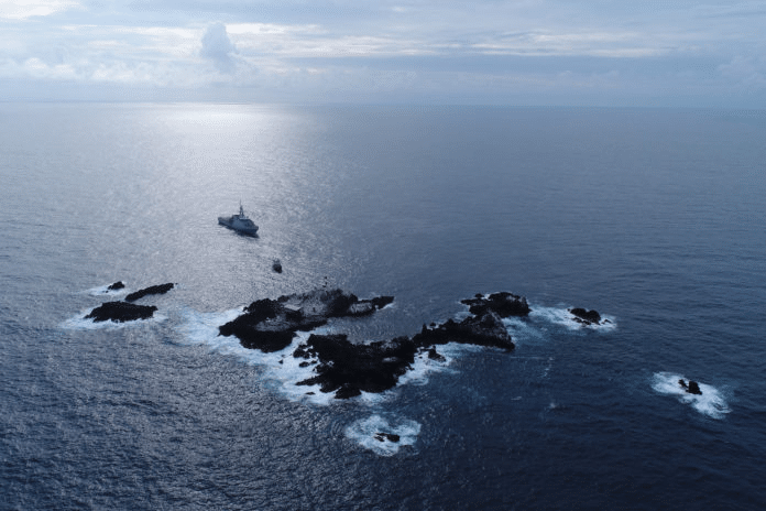 Ilha no oceano com navio ao fundo.