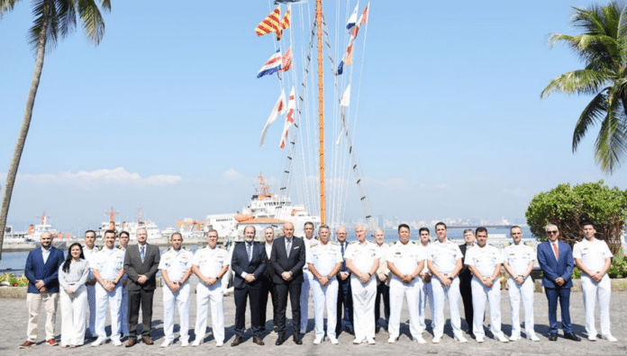 Autoridades navais reunidas em frente a navio e bandeiras.