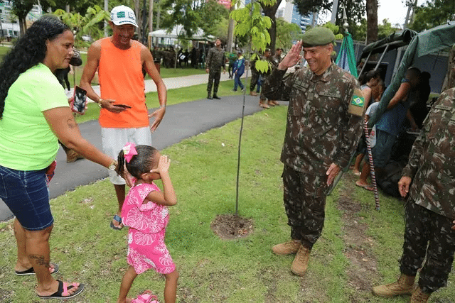 Criança saúda militar em uniforme no parque.