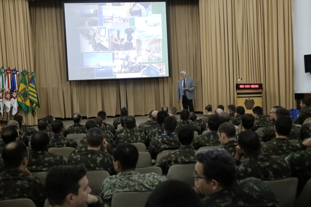 Palestra militar com slides e bandeiras ao fundo.