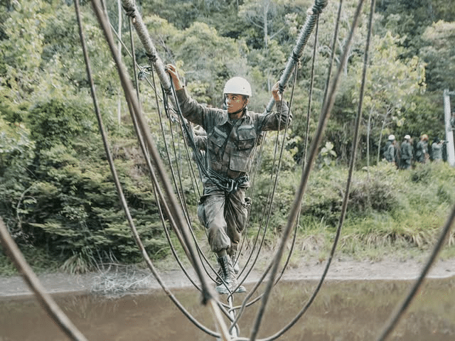 Soldado cruza ponte de cordas na selva.