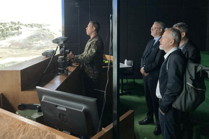 Militar opera simulador com observadores ao fundo.