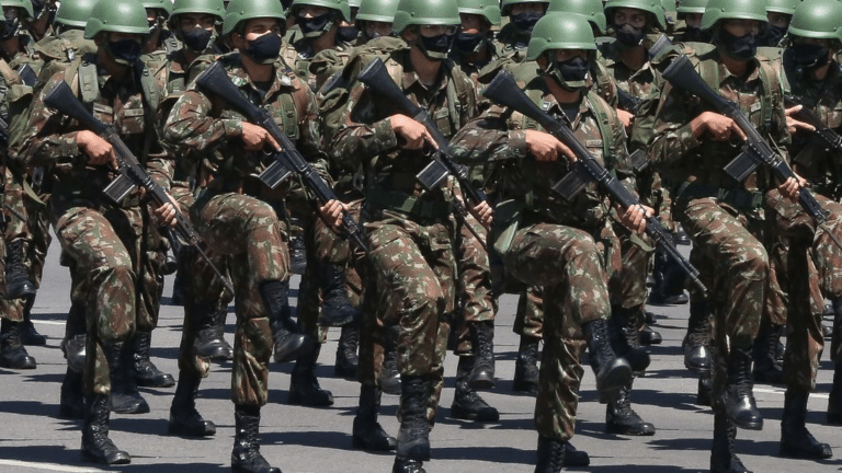 Soldados marcham em uniforme militar camuflado.