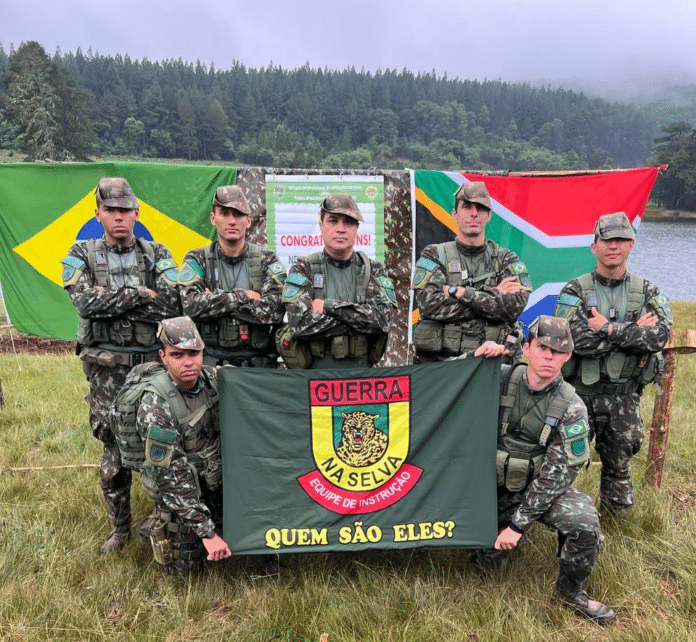 Soldados brasileiros em treinamento na selva, bandeira ao fundo.