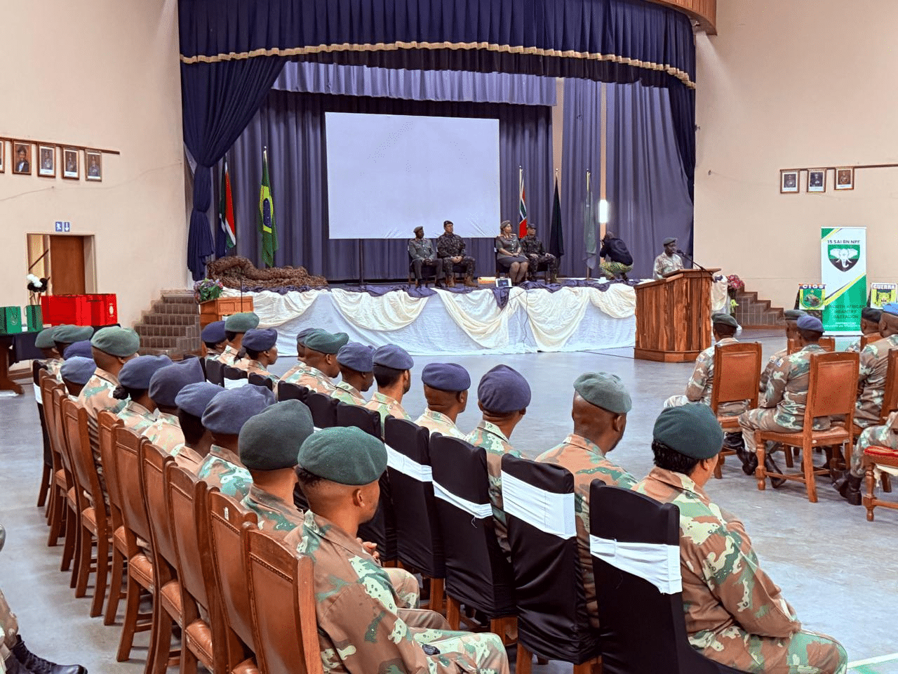 Cerimônia militar com soldados sentados em auditório.