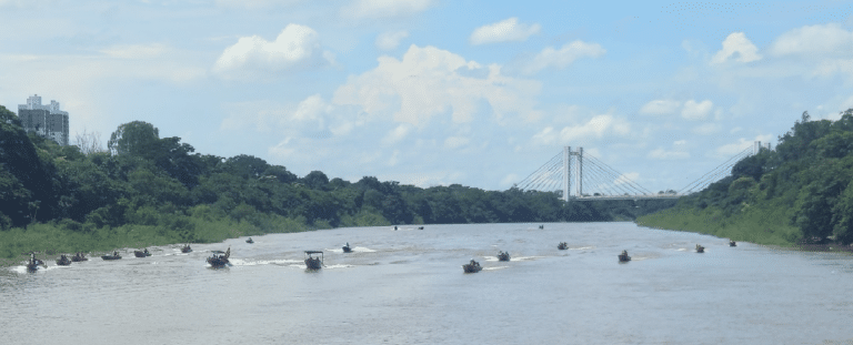Barcos navegando em rio com ponte ao fundo.