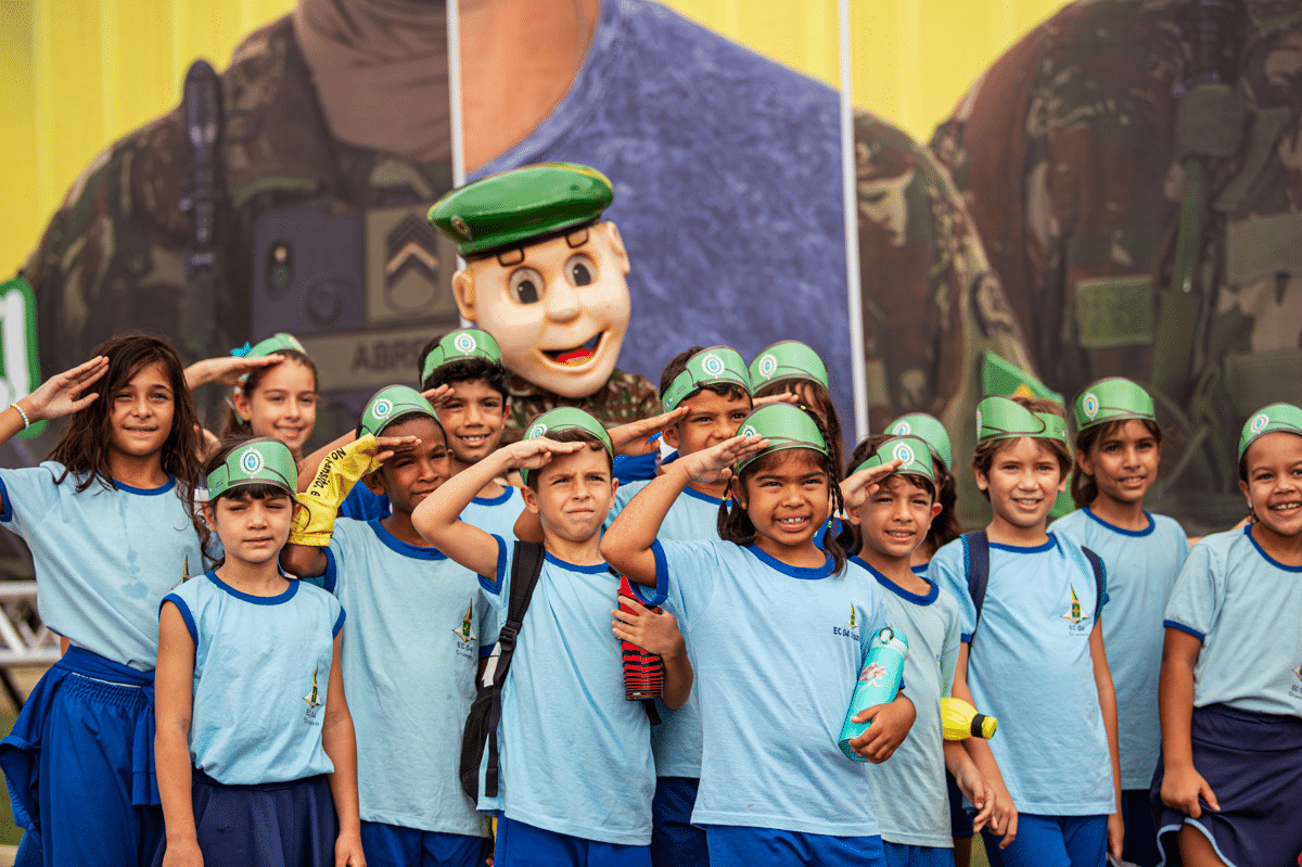 Crianças em uniforme escolar saudando ao ar livre.
