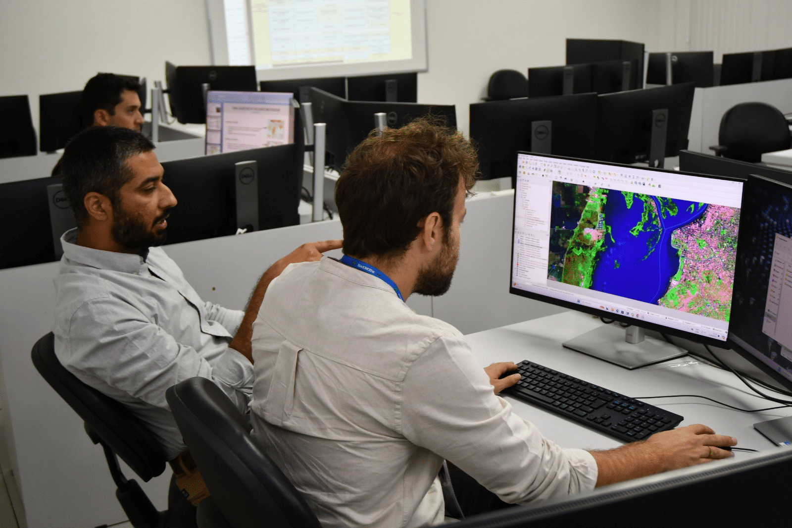 Homens analisando mapa em computadores no escritório.