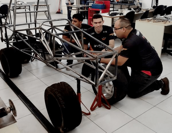 Estudantes trabalhando em chassi de carro de corrida.