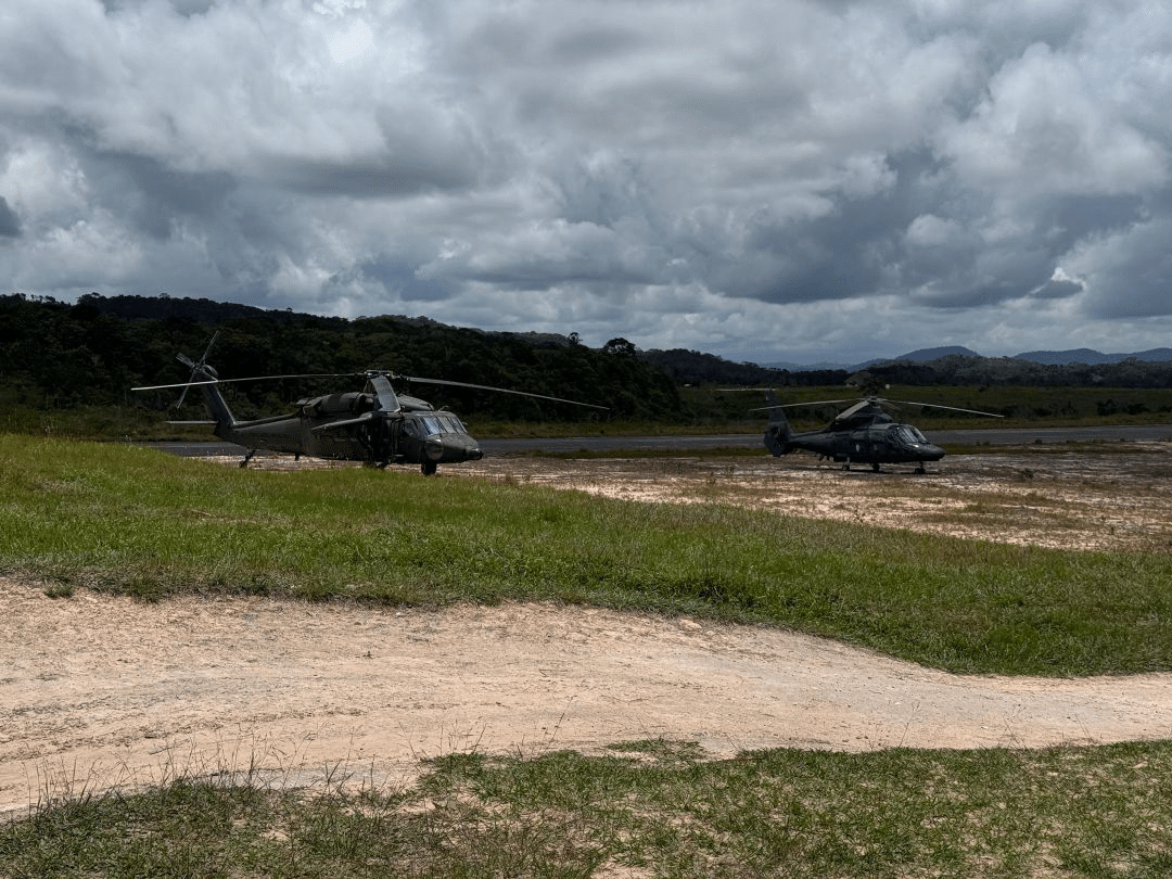 Helicópteros militares estacionados em campo aberto na selva.