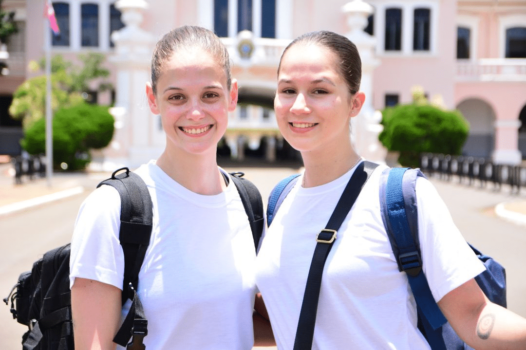 Duas estudantes sorridentes com mochilas na escola.