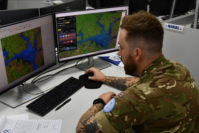 Soldado analisando mapas em dois monitores de computador.