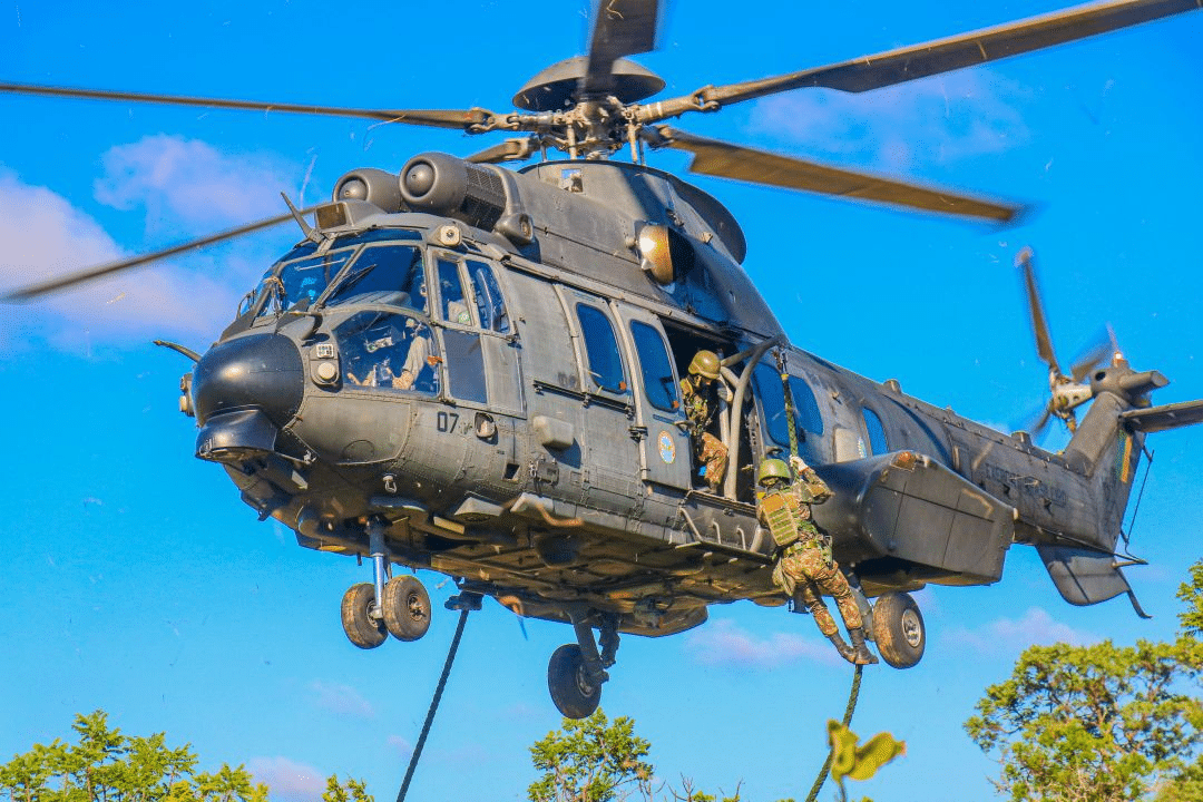 Helicóptero militar em operação com soldados descendo.