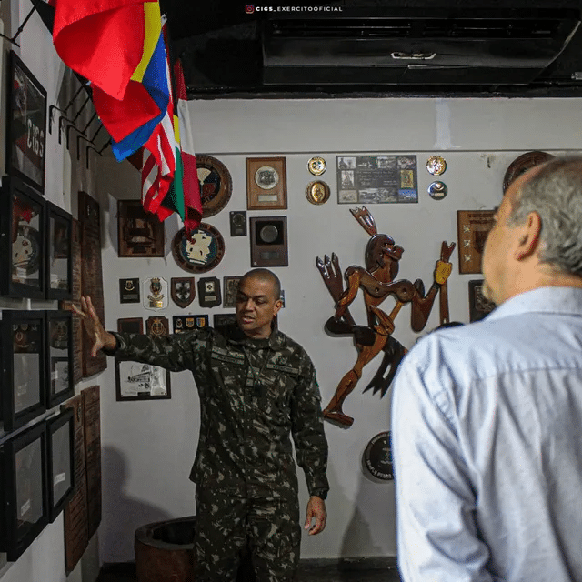 Militar explica prêmios em sala decorada com bandeiras.