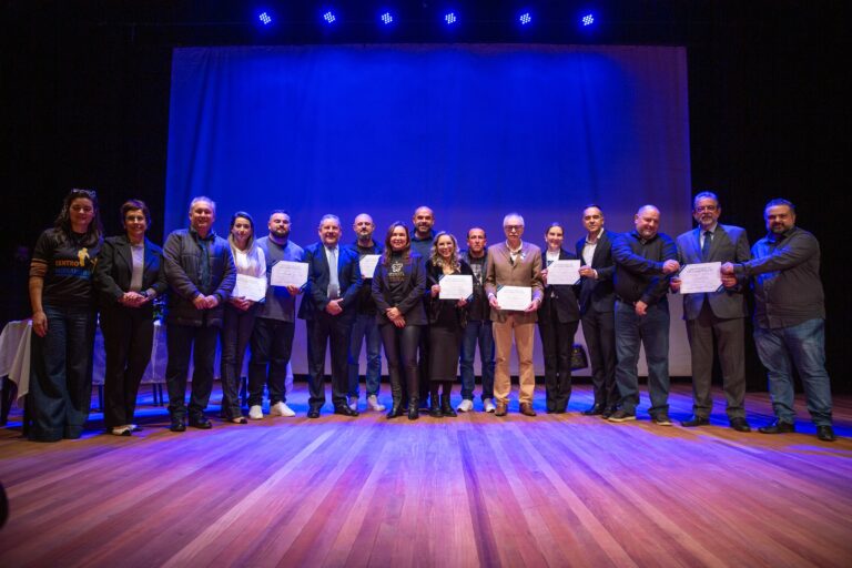 Grupo de pessoas segurando certificados em palco iluminado.