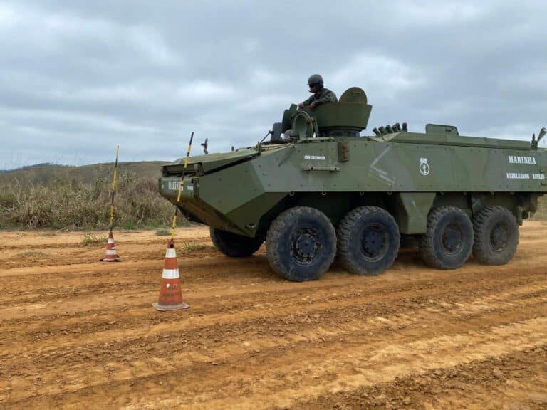 Tanque militar em estrada de terra com cones.