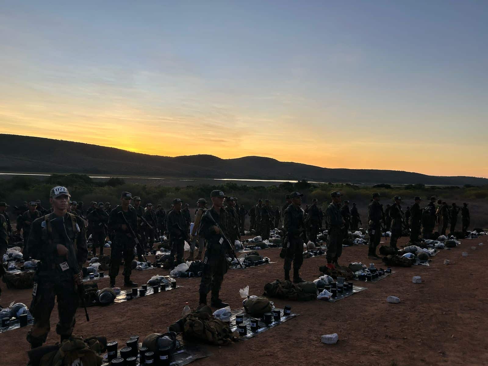 Soldados em fila com equipamentos ao pôr do sol.