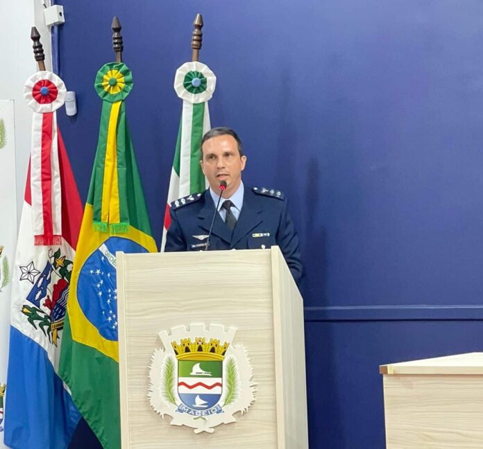 Oficial discursa em púlpito com bandeiras ao fundo.
