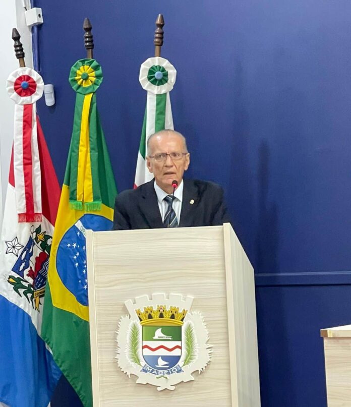 Homem discursando em púlpito com bandeiras ao fundo.