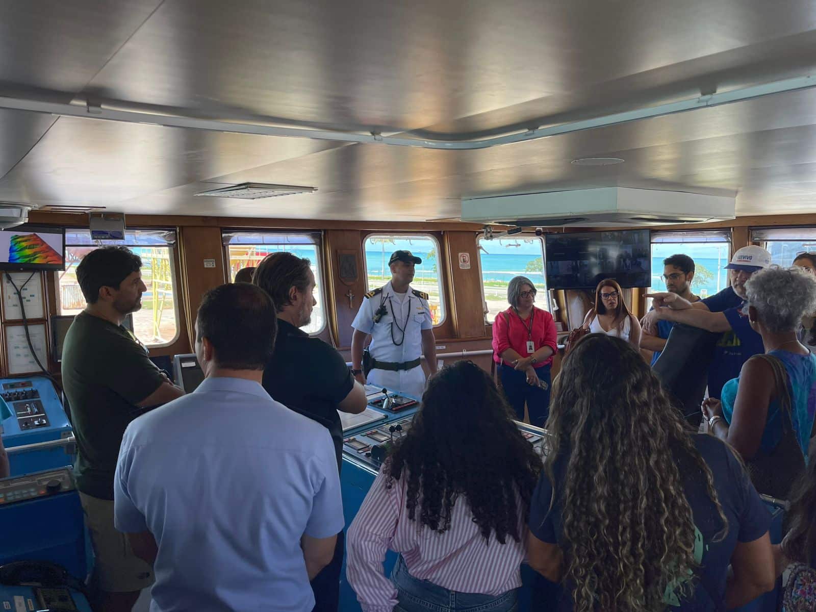 Pessoas reunidas em sala com janelas e vista para o mar.