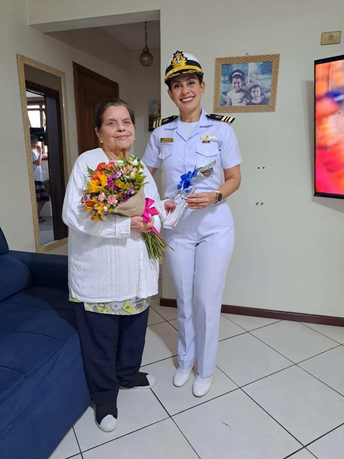 Idosa recebe flores de oficial da marinha em casa.