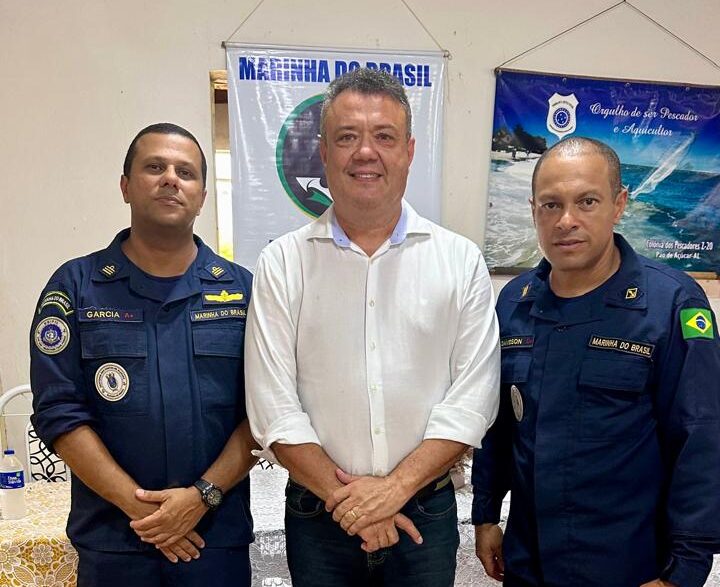 Três homens em frente a banners da Marinha do Brasil.