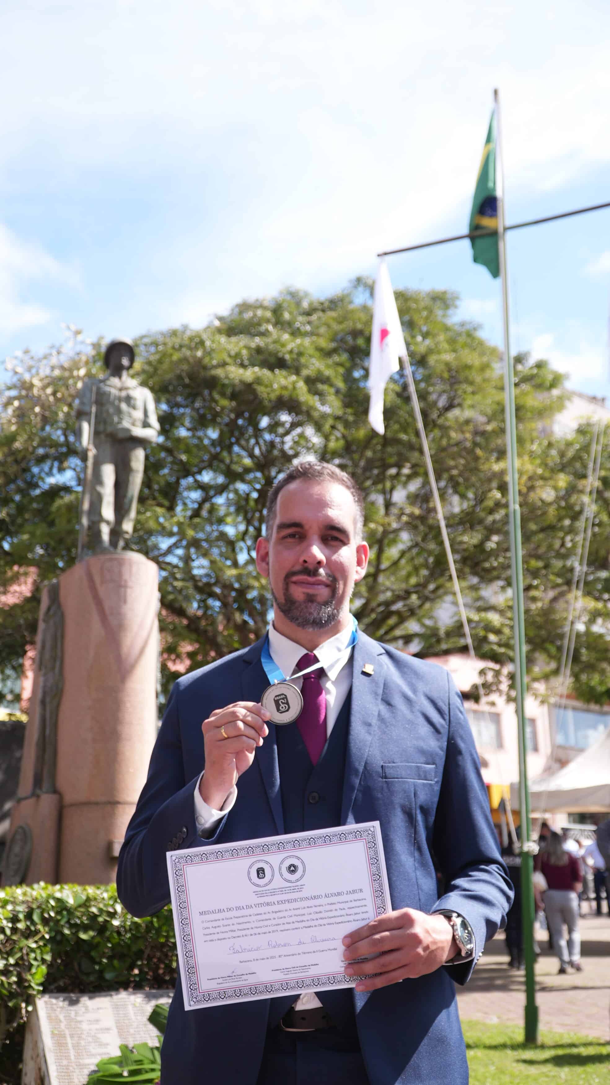 Homem com medalha e certificado, estátua ao fundo.