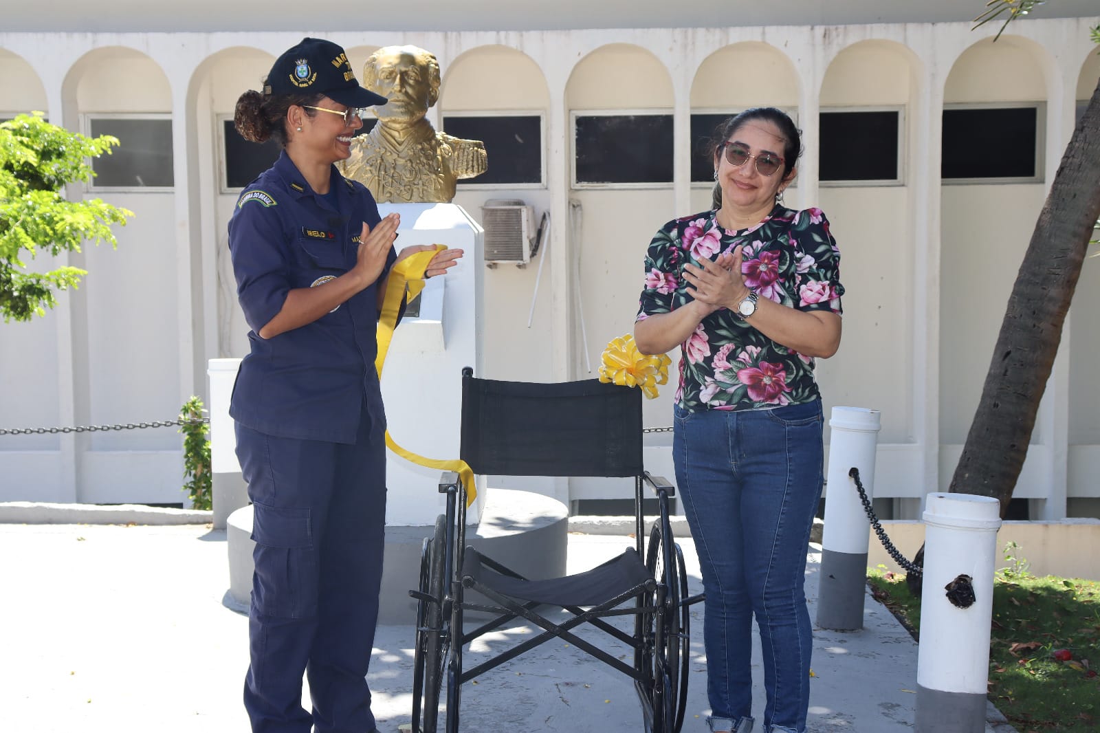 Duas mulheres sorriem ao lado de cadeira de rodas.
