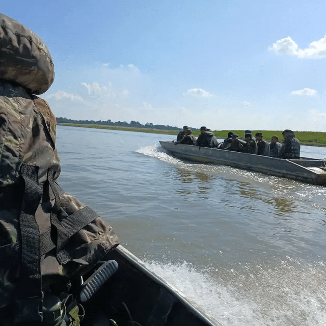 Militares em barcos navegando em rio sob céu azul.