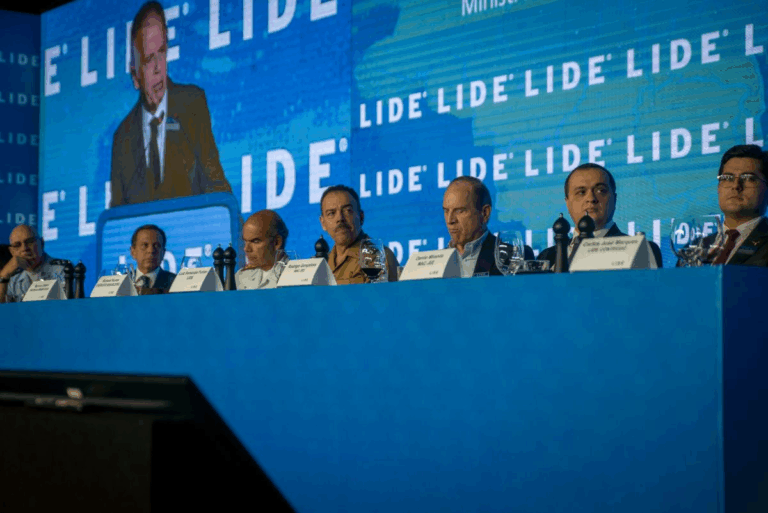 Palestrantes na conferência LIDE em mesa azul.