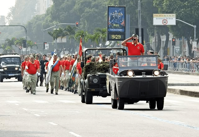 Desfile militar com veículos e pessoas uniformizadas.