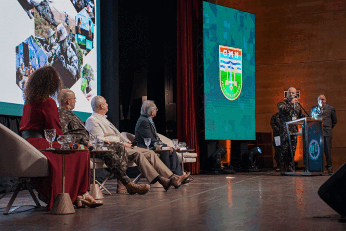 Palestra militar com painel e cinco participantes sentados.