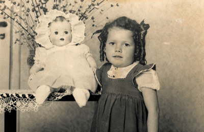 Menina em pé ao lado de boneca antiga.